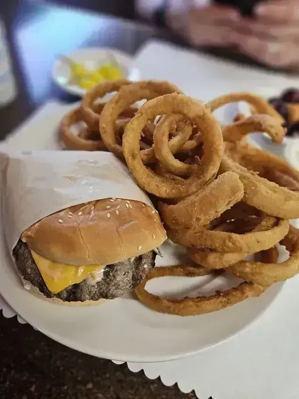 A cheeseburger in paper wrap with a pile of onion rings at Harry's Cafe, Katella Ave, Stanton, CA