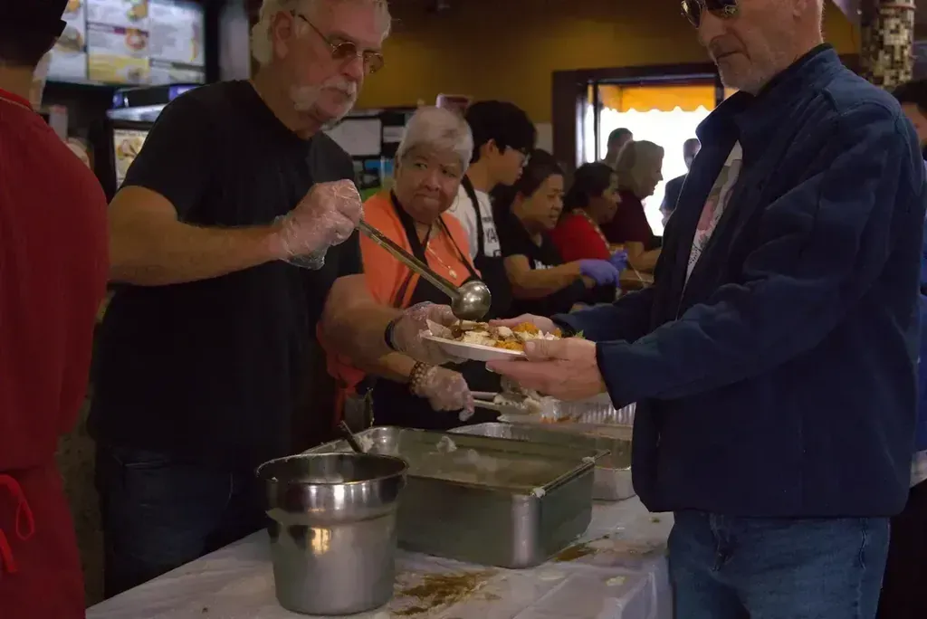 A volunteer serving a plate to a guest at the Thanksgiving serving line at Harry's Cafe, Katella Ave, Stanton, CA