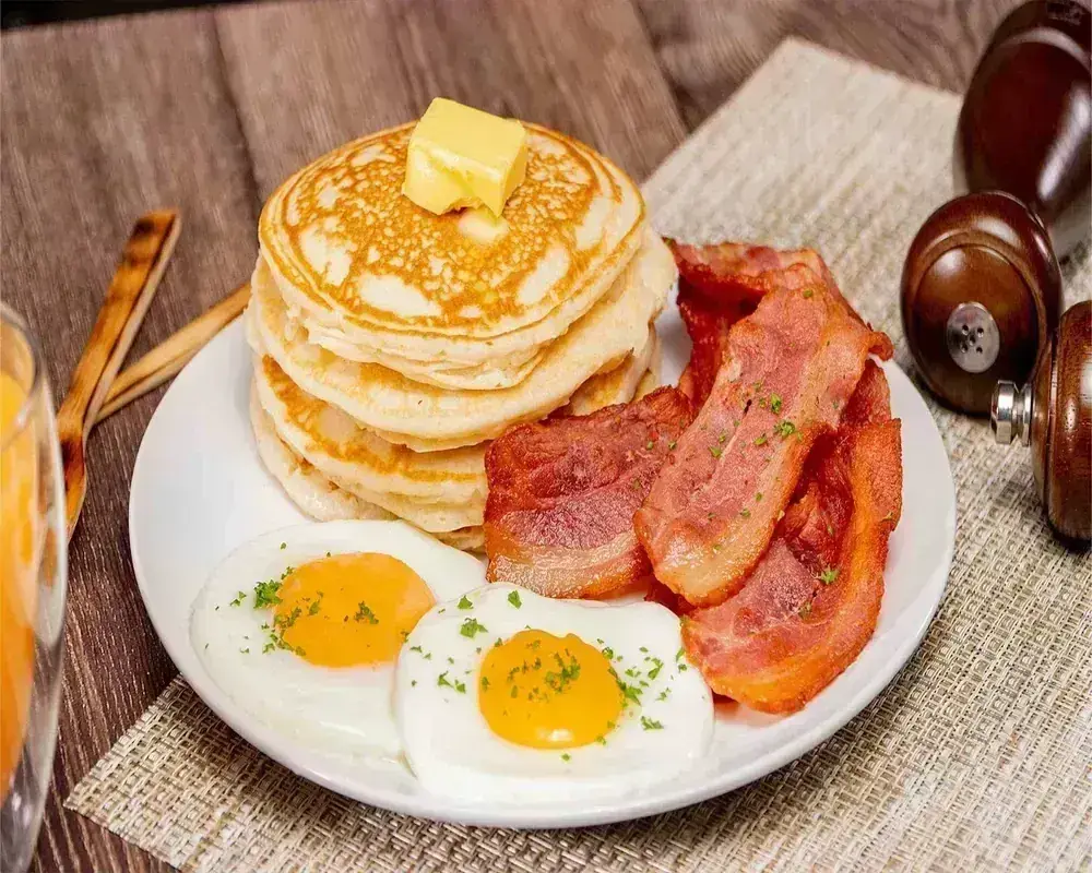 A stack of pancakes with butter beside bacon and two eggs at Harry's Cafe, Katella Ave, Stanton, CA