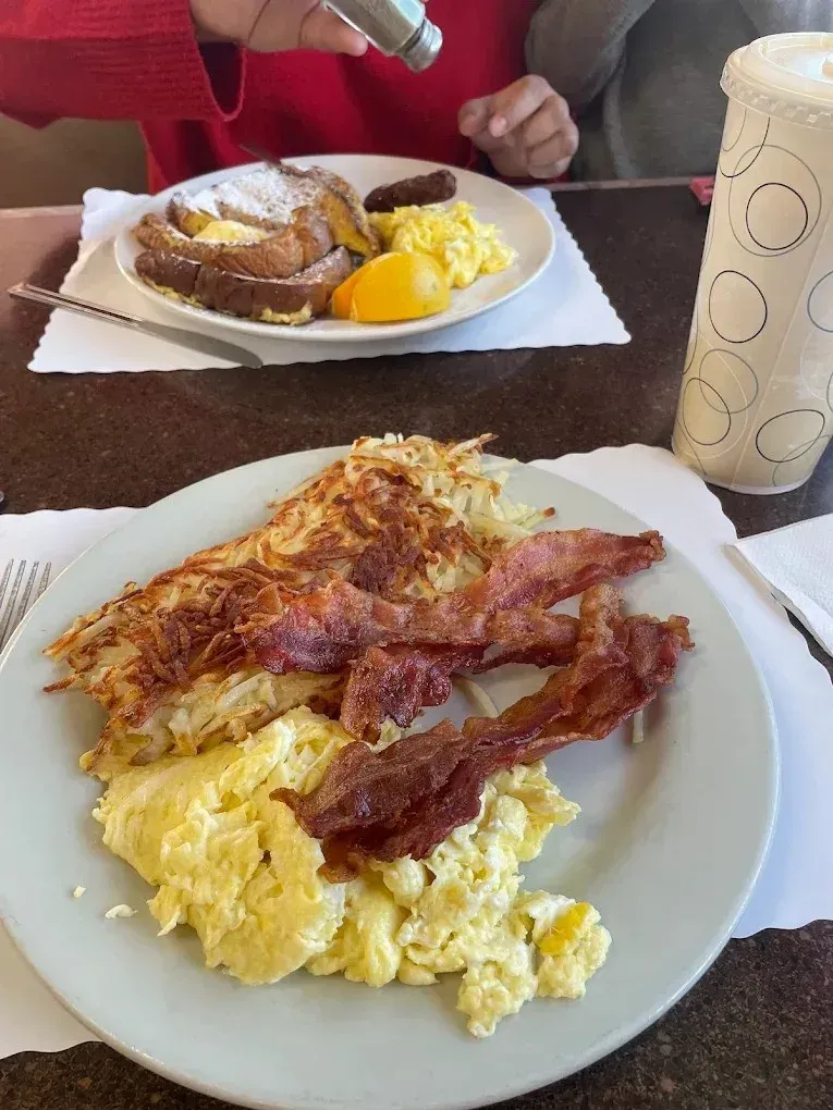 A stack of pancakes with butter, two fried eggs, and strips of bacon on a plate at Harry’s Cafe, Katella Ave, Stanton, CA.